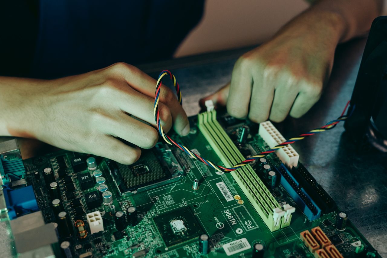 gallery-5 Person assembling computer motherboard with colorful wires, showcasing technology and engineering.